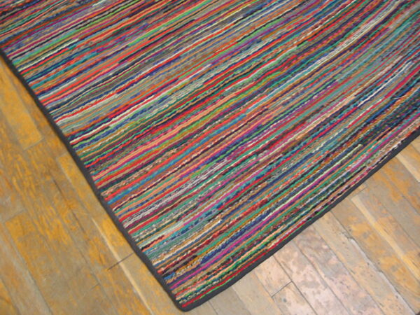 Multicolor low-profile rug with thin linear stripes resting on worn light wood flooring.