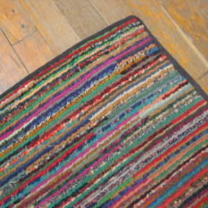 A high-texture rug with thick diagonal rainbow stripes sits on distressed light wood flooring.