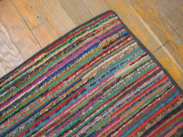 A high-texture rug with thick diagonal rainbow stripes sits on distressed light wood flooring.