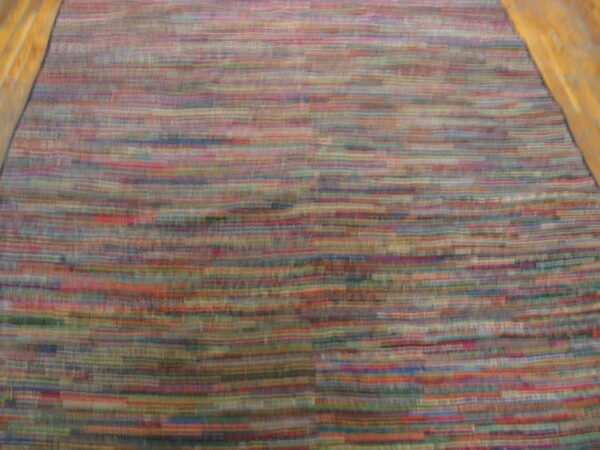 Multicolored rug with blurred horizontal stripes in red, blue, and green, flanked by golden wood floor.