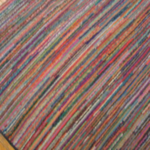 A flatweave rug with thin, multicolored diagonal stripes covers a section of light wood floor.
