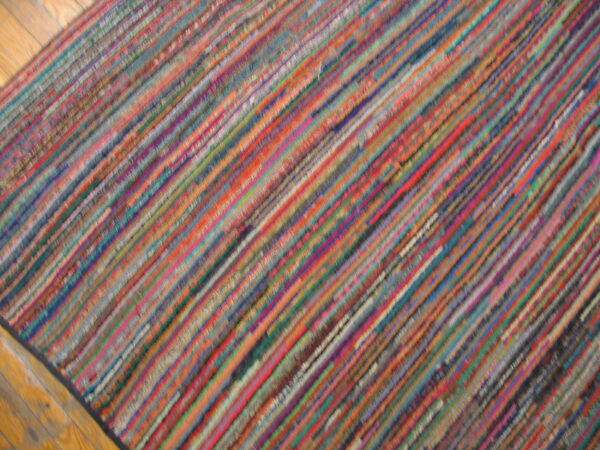 A flatweave rug with thin, multicolored diagonal stripes covers a section of light wood floor.