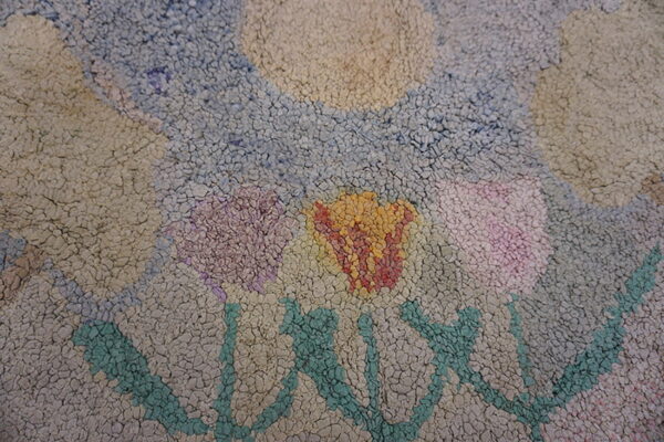 Close-up of a chunky, textured rug showing an abstract floral pattern in pastel colors on a light background.
