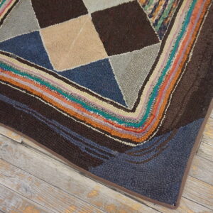 Multicolored geometric rug corner with brown, blue, and tan shapes framed by a chunky striped border on wood floor.
