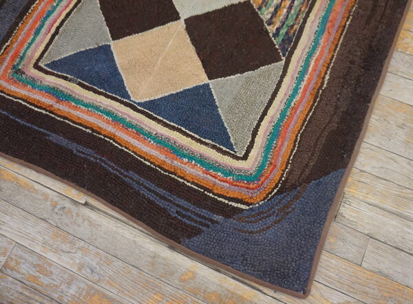 Multicolored geometric rug corner with brown, blue, and tan shapes framed by a chunky striped border on wood floor.