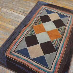 Textured rug with multi-color geometric diamond design and striped border on worn wood planks.