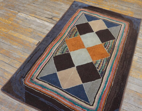 Textured rug with multi-color geometric diamond design and striped border on worn wood planks.
