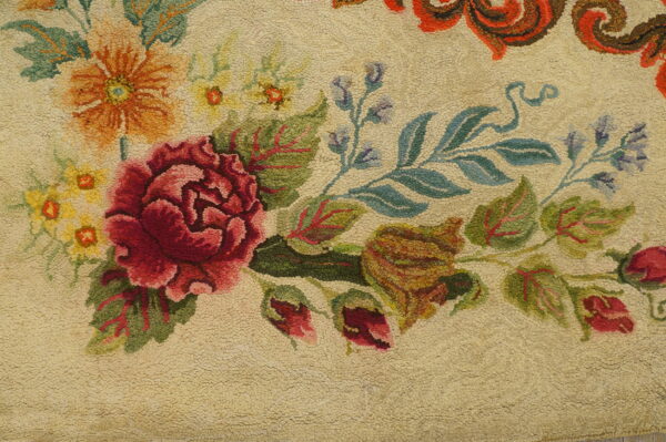 Loop-pile rug detail showing large crimson, orange, and green flowers on a textured cream field.