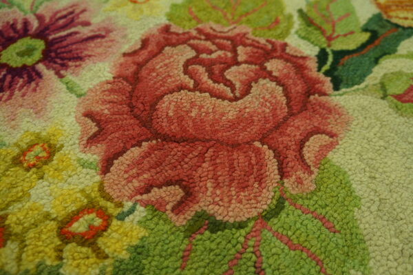 Close-up of a tightly looped rug pile depicting a pink rose, yellow flowers, and bright green leaves.