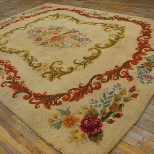 Cream rug with a colorful floral center and intricate rust and green scrolling borders on plank flooring.