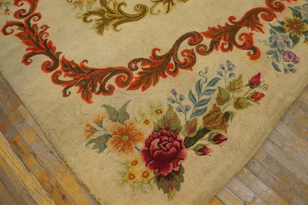 Beige low-pile rug featuring red roses and intricate floral and scrolling patterns on worn wood flooring.