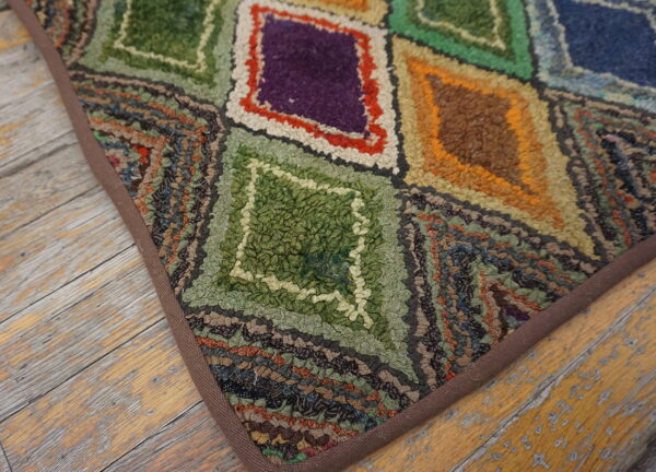 Textured, multicolored rug with geometric diamond shapes sits on distressed light wood flooring.