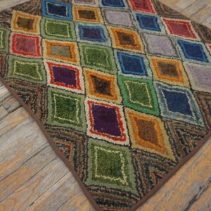 Multicolor hooked rug featuring bright diamond patterns rests on rustic, worn wood flooring.