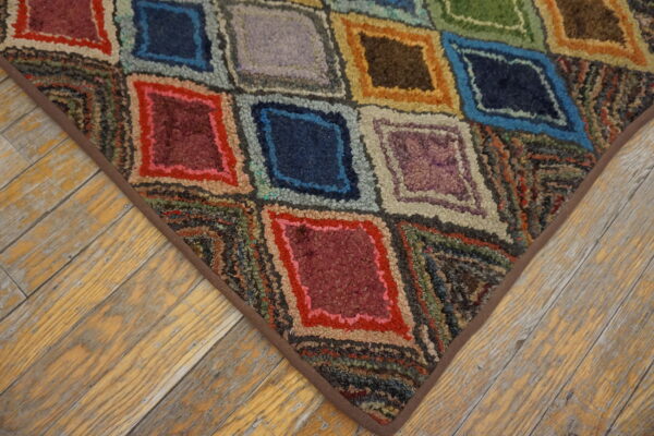 Multicolored hooked rug with diamond patterns and a brown border on distressed wood floors.