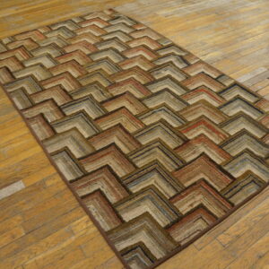 Textured rug featuring a layered chevron pattern in multi-tonal earth tones on distressed wooden flooring.