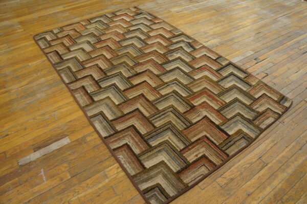 Textured rug featuring a layered chevron pattern in multi-tonal earth tones on distressed wooden flooring.