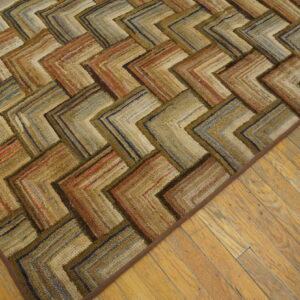Textured rug showing a multicolored chevron pattern in browns, rusts, and blues on distressed wood flooring.