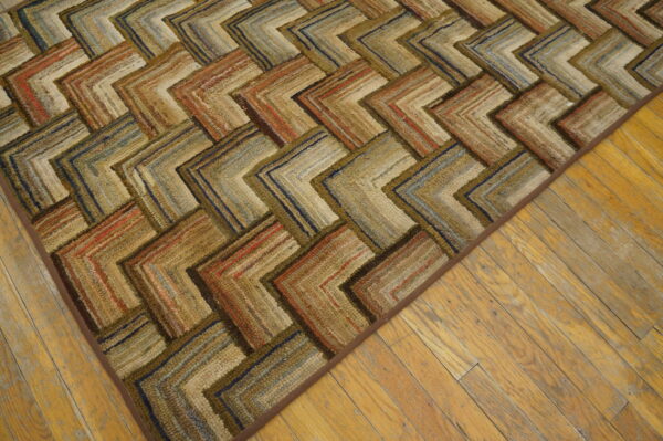 Textured rug showing a multicolored chevron pattern in browns, rusts, and blues on distressed wood flooring.