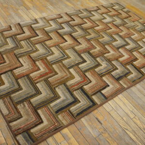 Geometric textured rug in variegated brown, tan, orange, and blue zigzags rests on light wood planks.