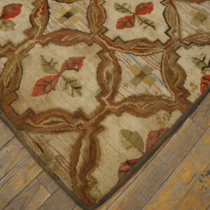 Close-up of a textured cream rug featuring brown lattice work and rust red leaf motifs on distressed wood floors.