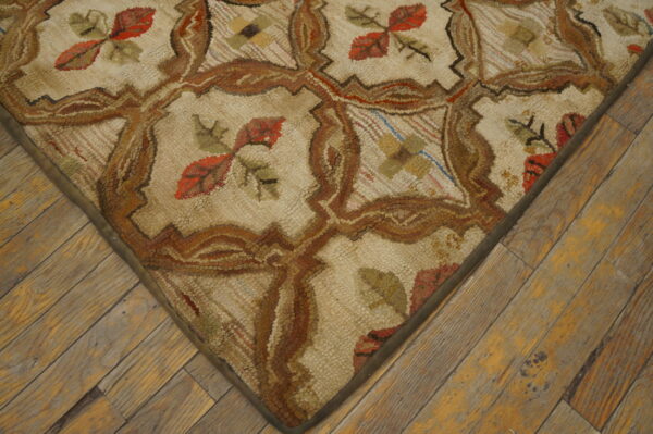 Close-up of a textured cream rug featuring brown lattice work and rust red leaf motifs on distressed wood floors.