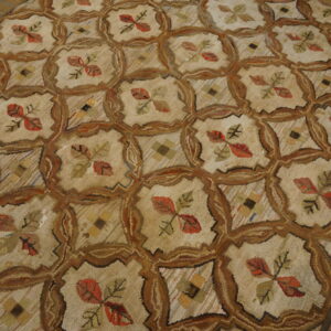 Textured beige rug featuring a brown lattice pattern enclosing red leaves and small geometric designs on wood flooring.