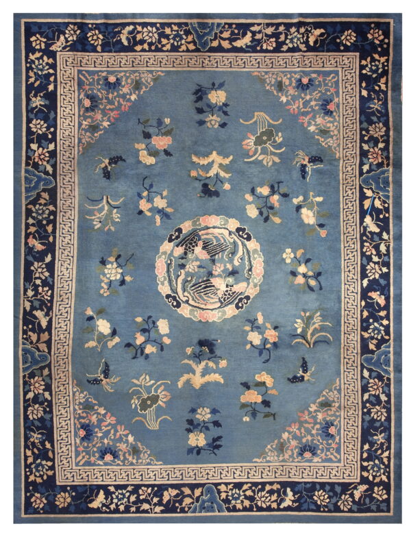 Medium blue rug featuring scattered flowers, a central bird design, and a navy border with a greek key band.