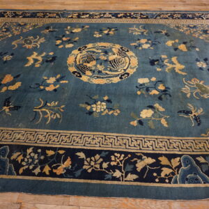 Deep blue rug with gold, peach, and navy floral patterns and intricate geometric borders on wood flooring.