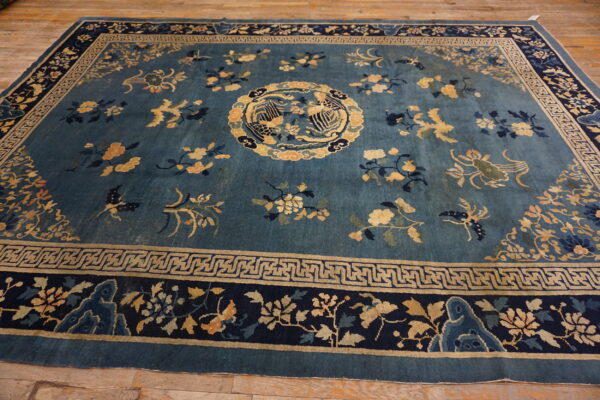 Deep blue rug with gold, peach, and navy floral patterns and intricate geometric borders on wood flooring.