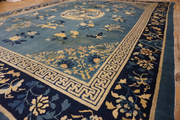 Teal and navy blue rug with gold floral and geometric patterns visible on wood flooring.