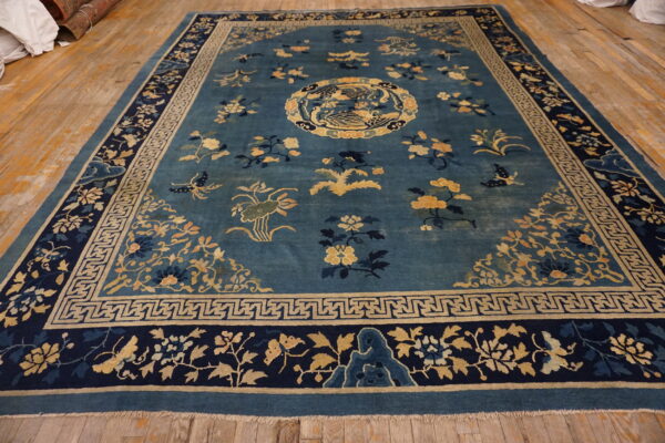 Teal rug with gold and navy botanical patterns, a central bird, and fretwork borders on light wood flooring.