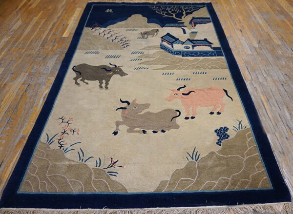 Deep navy bordered rug with a pastoral scene of oxen, hills, and blue buildings on distressed wood plank floors.
