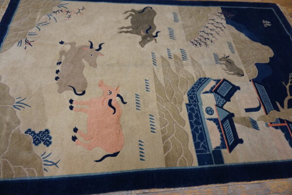 Beige and navy rug featuring oxen and a pink pig in a stylized scenic landscape on wood planks.