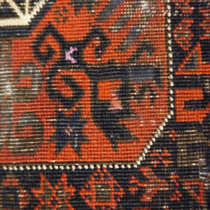 Low-pile rug close-up featuring dense geometric patterns in red, black, dark blue, and cream.