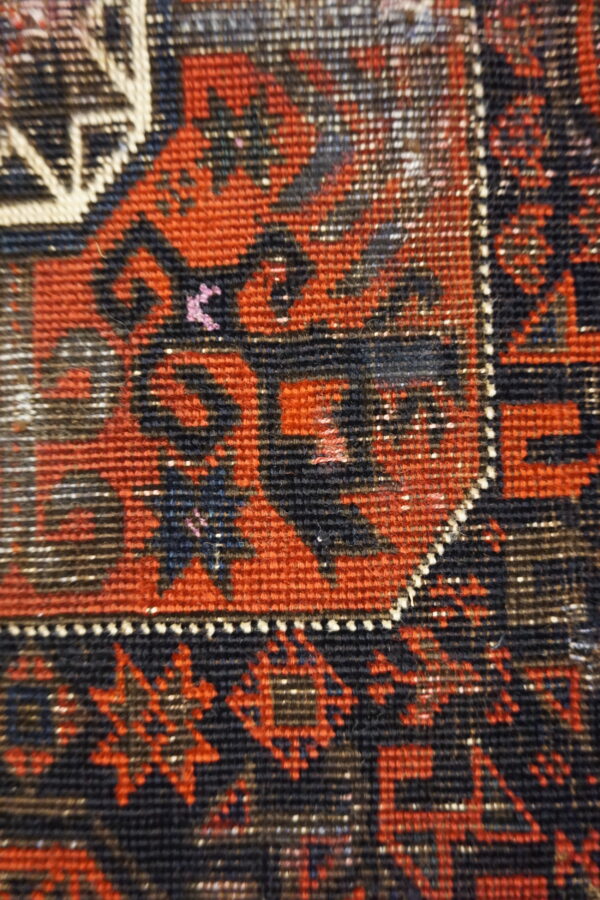 Low-pile rug close-up featuring dense geometric patterns in red, black, dark blue, and cream.