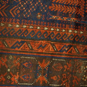 Navy blue and rust red patterned rug featuring multiple borders of geometric motifs over wood planks.