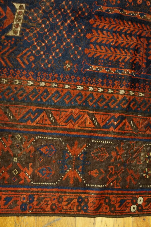 Navy blue and rust red patterned rug featuring multiple borders of geometric motifs over wood planks.