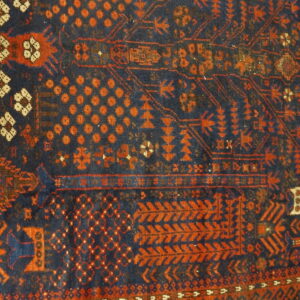 Traditional blue and rust orange rug detail featuring dense geometric motifs and patterned horizontal borders.