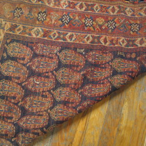 Closeup of a traditional rug with rust and navy paisley motifs curled over worn hardwood floors.