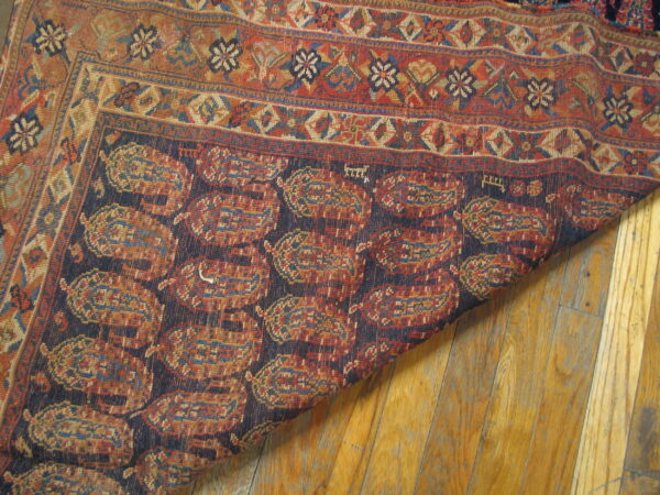Closeup of a traditional rug with rust and navy paisley motifs curled over worn hardwood floors.