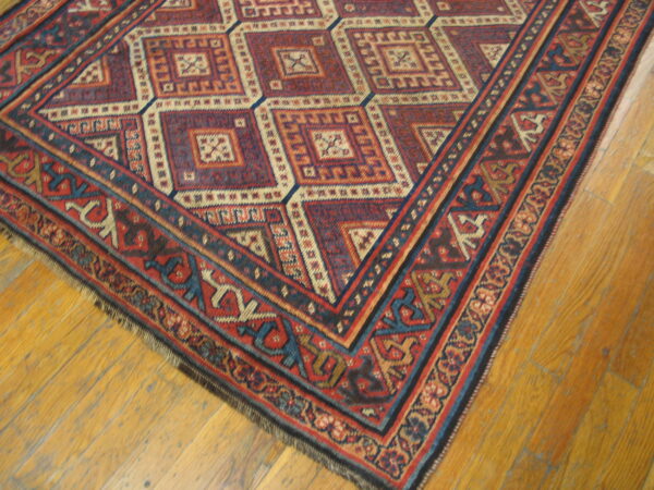 Red, navy, and cream geometric rug with complex borders on distressed wood plank flooring.