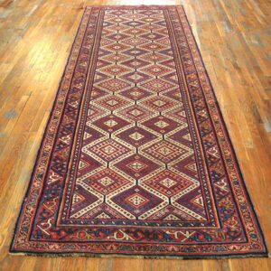 Red, navy, and cream geometric runner with repeating diamond patterns on light brown wood flooring.