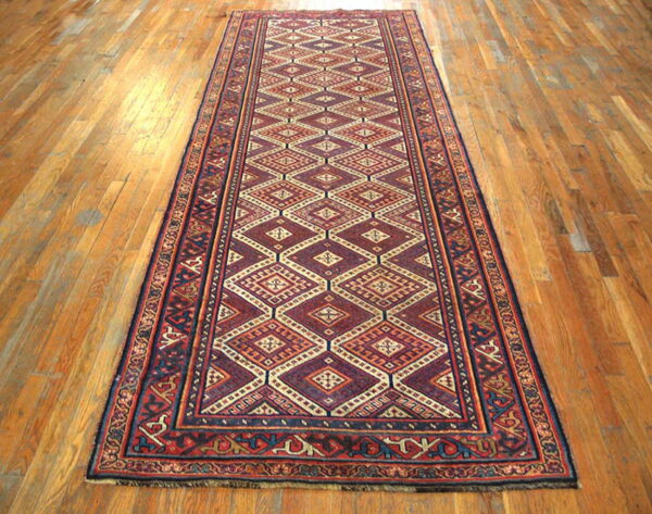 Red, navy, and cream geometric runner with repeating diamond patterns on light brown wood flooring.