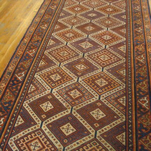 Detailed low-pile runner rug with large diamond patterns in rust, dark blue, and cream sits on wood planks.
