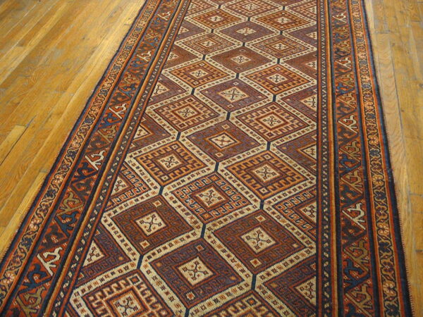 Detailed low-pile runner rug with large diamond patterns in rust, dark blue, and cream sits on wood planks.