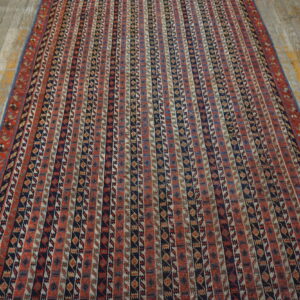 Vertical patterned rug in red, navy, and tan colors on gray wood plank flooring.