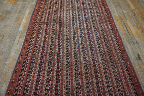Vertical patterned rug in red, navy, and tan colors on gray wood plank flooring.