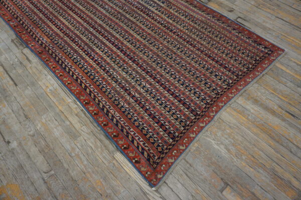 A striped rug in rust, navy, and beige with a patterned red border rests on worn wood flooring.