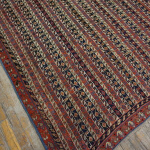 Red and navy rug with geometric vertical stripes lies on rustic, distressed wood plank flooring.