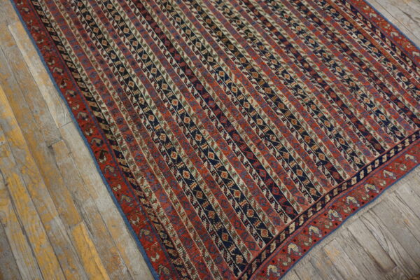 Red and navy rug with geometric vertical stripes lies on rustic, distressed wood plank flooring.